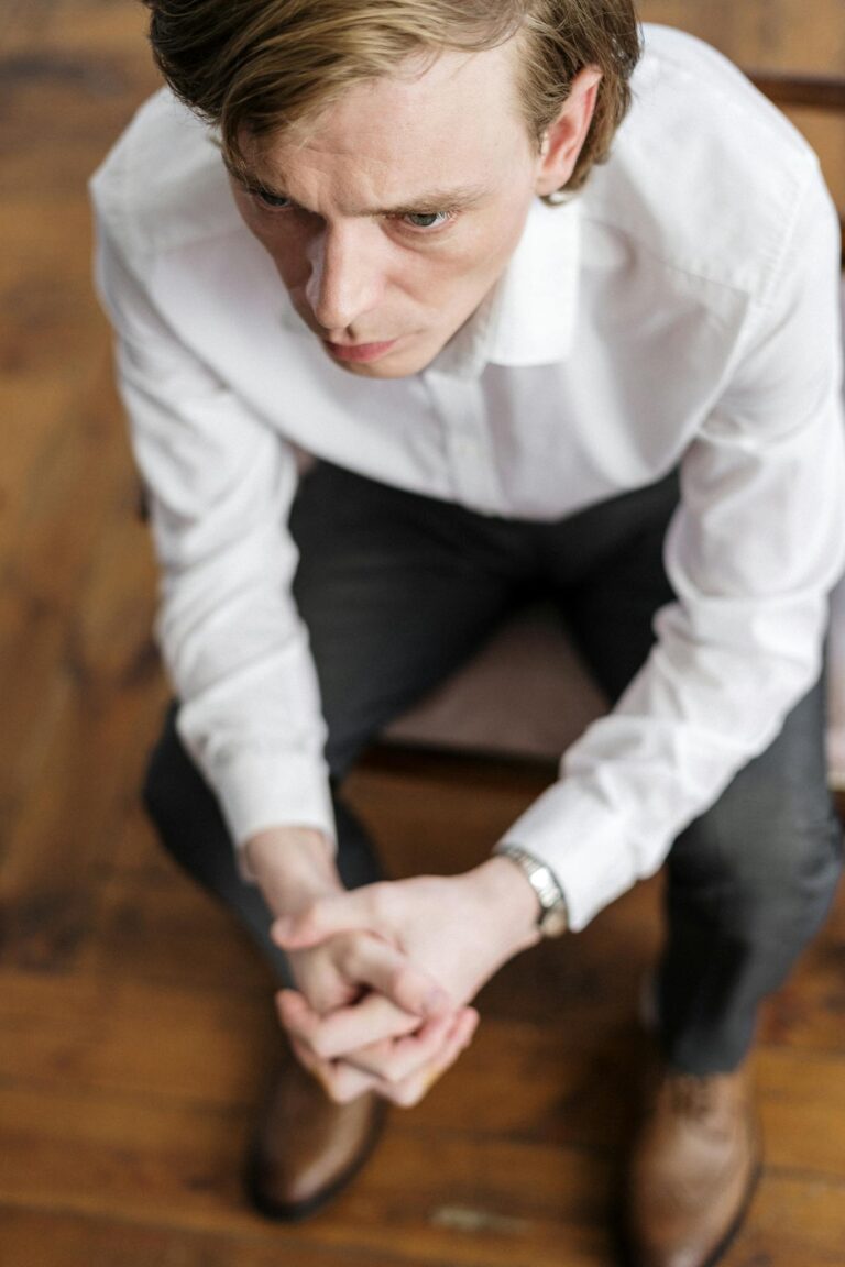 Man in deep thought sitting on a chair in an indoor setting wearing formal attire.
